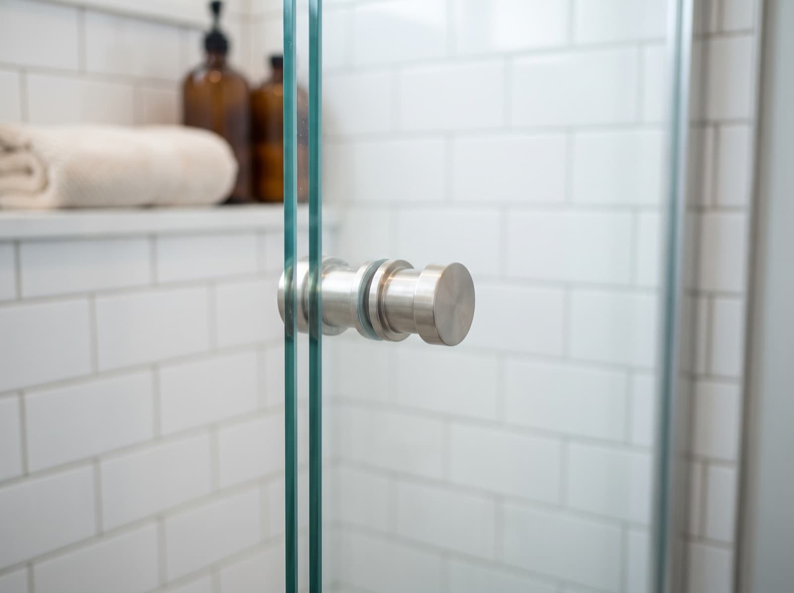 Close-up of a brushed nickel pull handle mounted through frameless shower glass