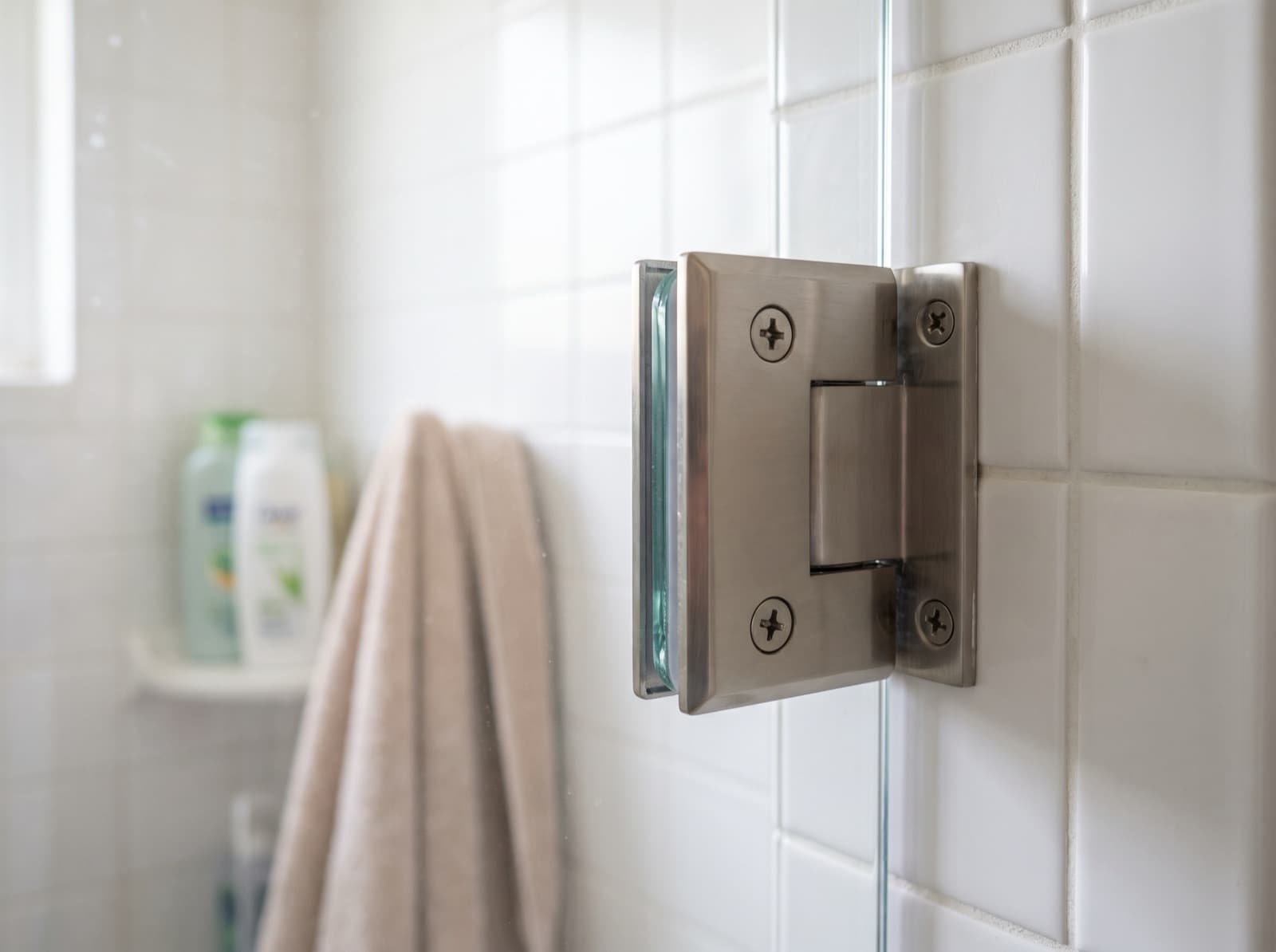 Close-up of a brushed nickel wall hinge clamping a frameless glass shower door