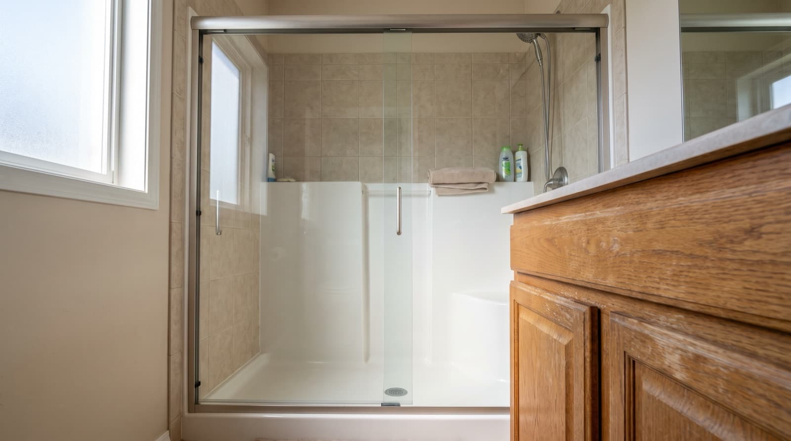 Semi-frameless glass shower door with a slim metal frame beside an oak vanity