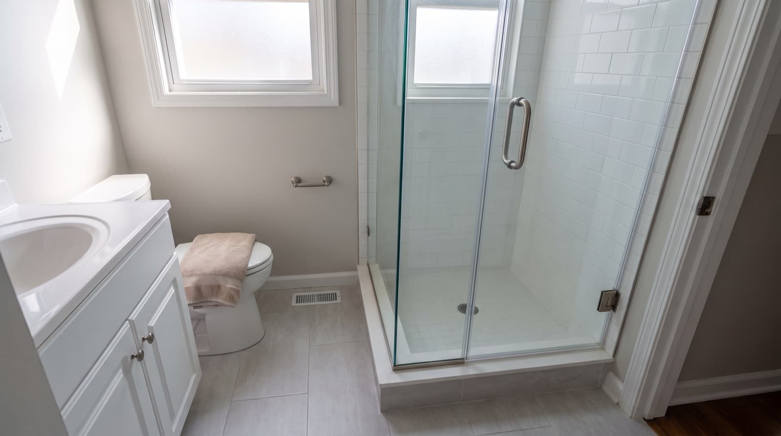 Frameless clear glass shower door with a brushed nickel handle in a white tile bathroom
