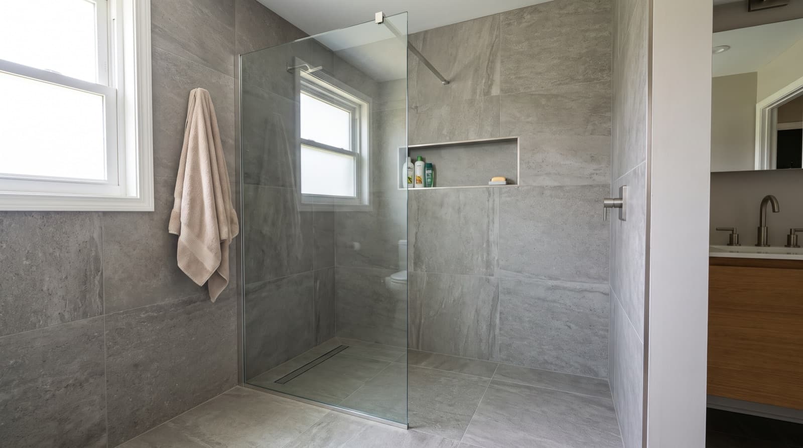 Fixed frameless glass panel on a curbless walk-in shower with gray tile