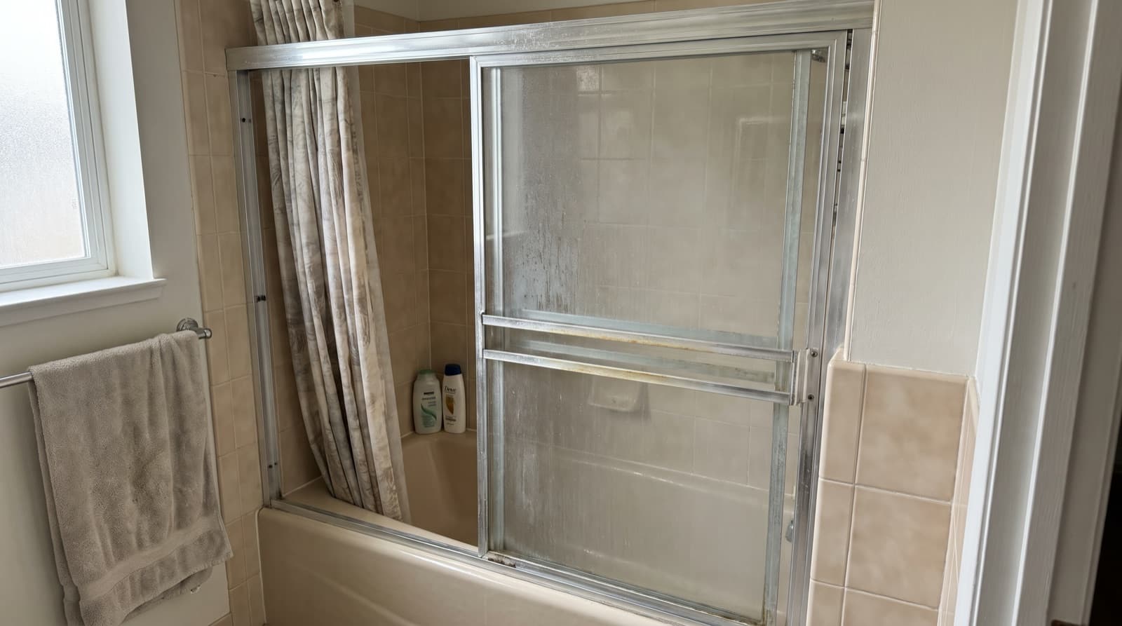 Older framed sliding shower door over a tub, with hard water spots on the glass